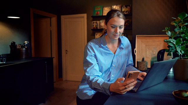 Woman in kitchen with computer and mobile.